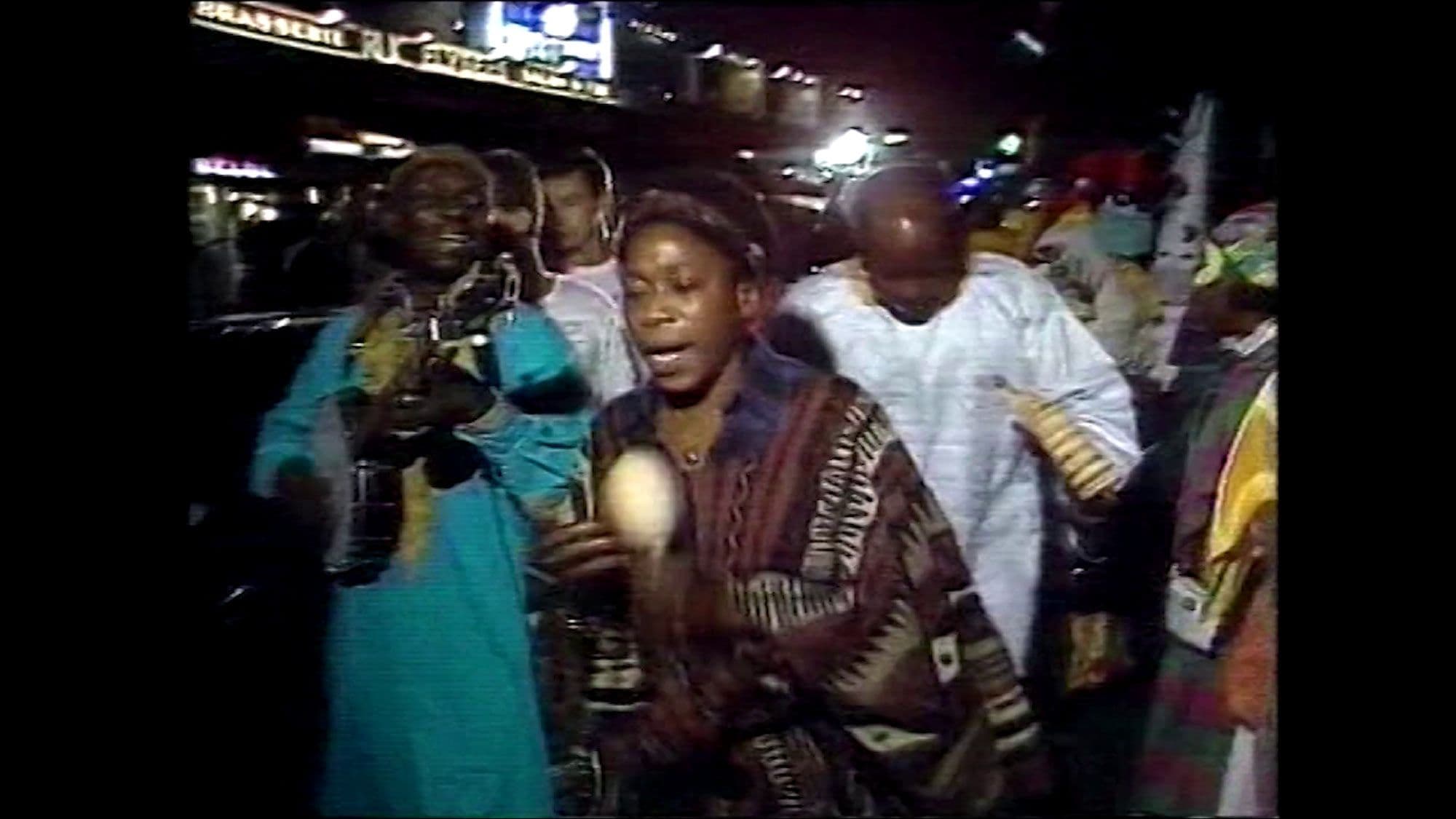 A group of people walking down a street at night while playing music.